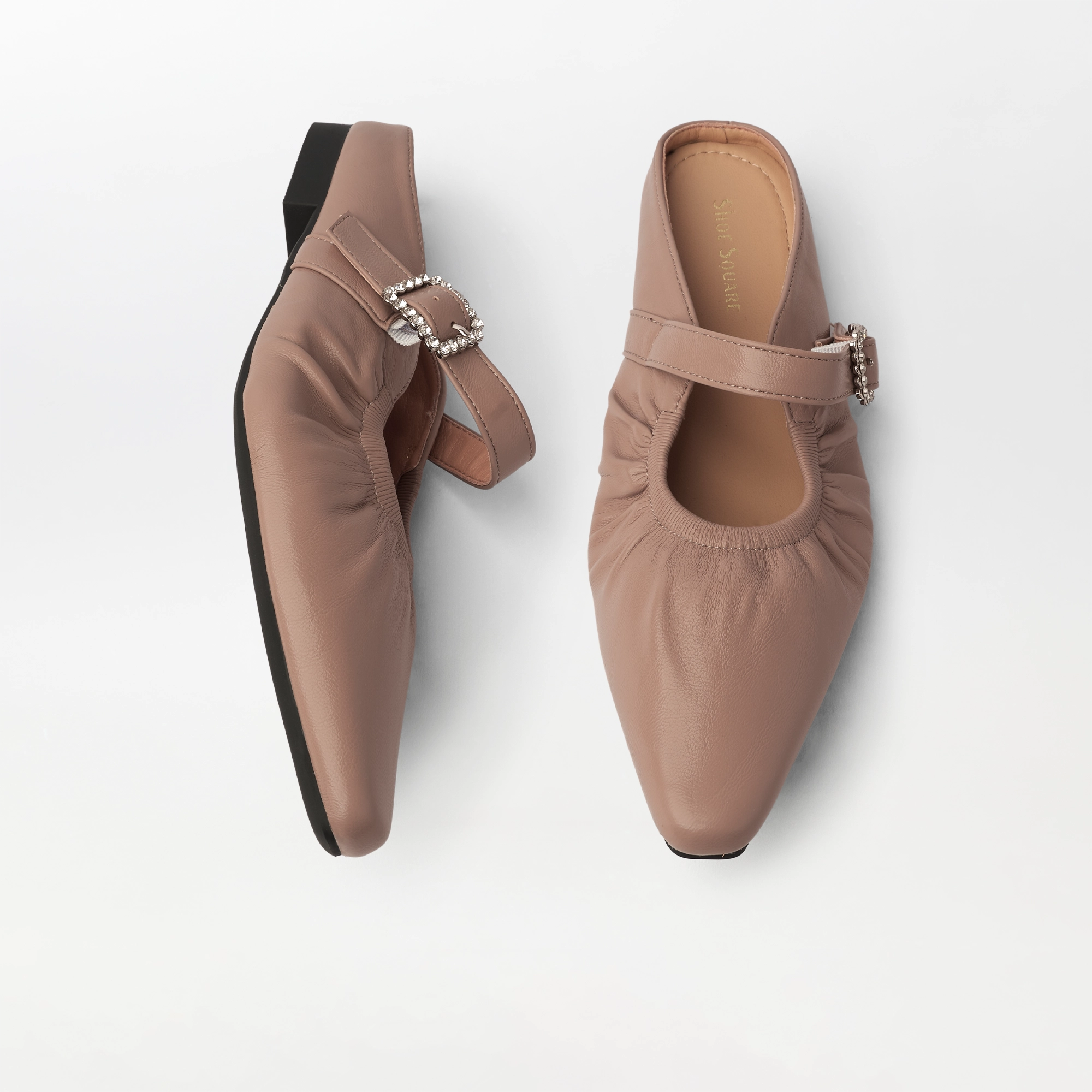 A pair of pointed-toe Mary Jane mules in a dusty blush pink leather, featuring a decorative rhinestone-embellished buckle strap and a black outsole, shown from two angles on a light gray background.