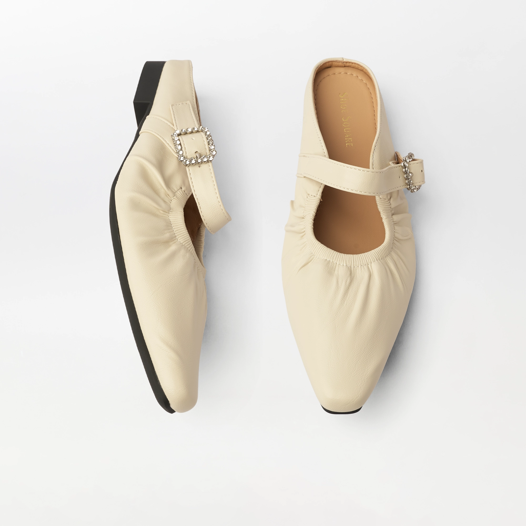 A pair of cream-colored Mary Jane flat shoes with gathered fabric uppers, pointed toes, and decorative rhinestone-embellished buckle straps, shown from top and side angles on a light gray background.